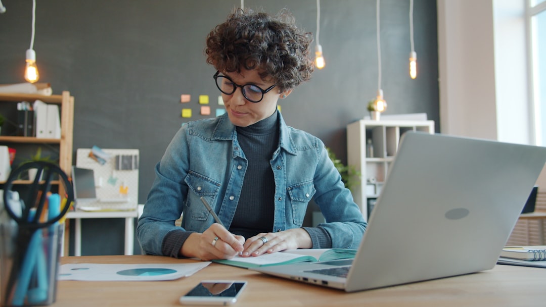 Woman with curly hair writing at desk with laptop